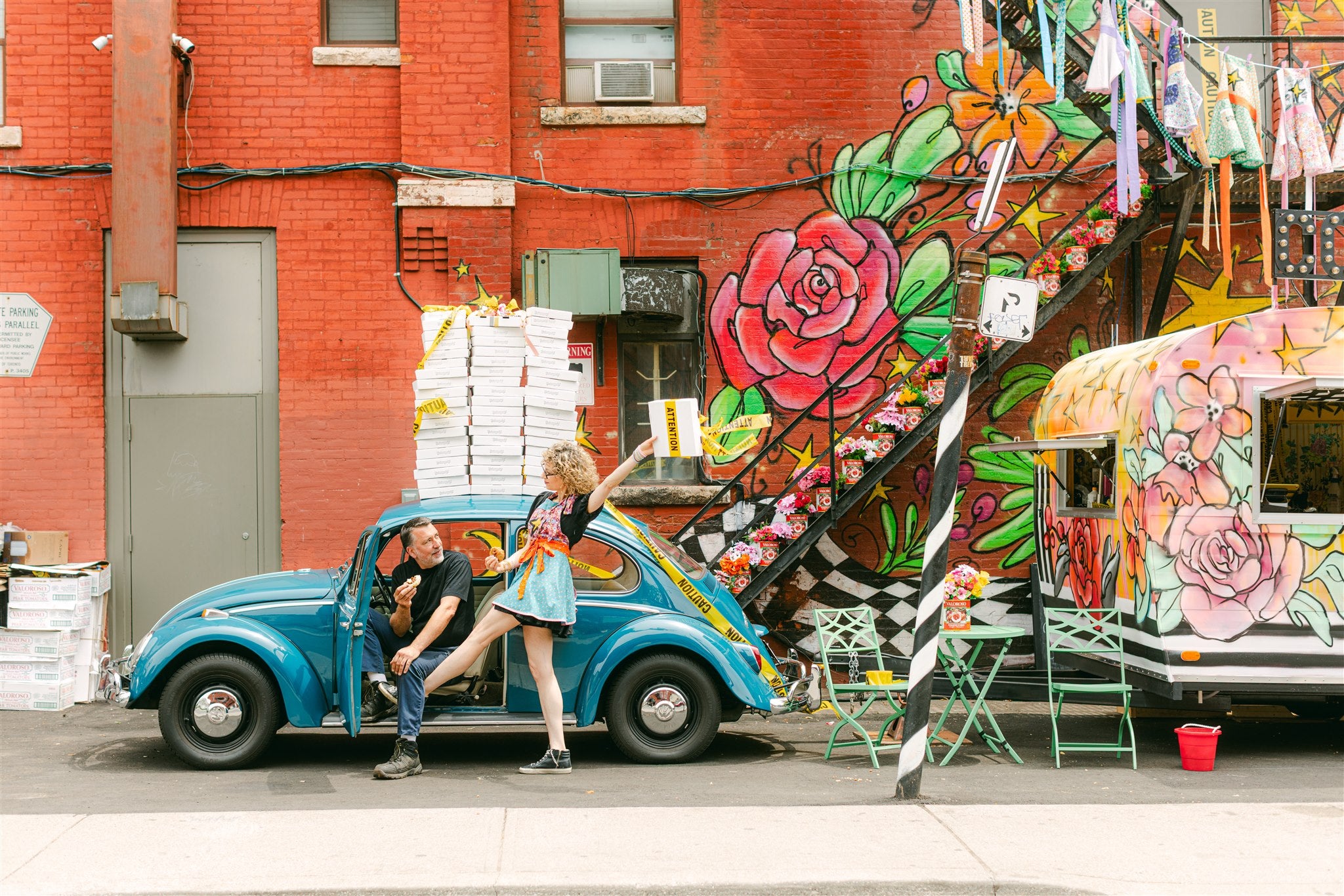 Couple sitting in a vintage blue car with colorful floral decorations on a street.