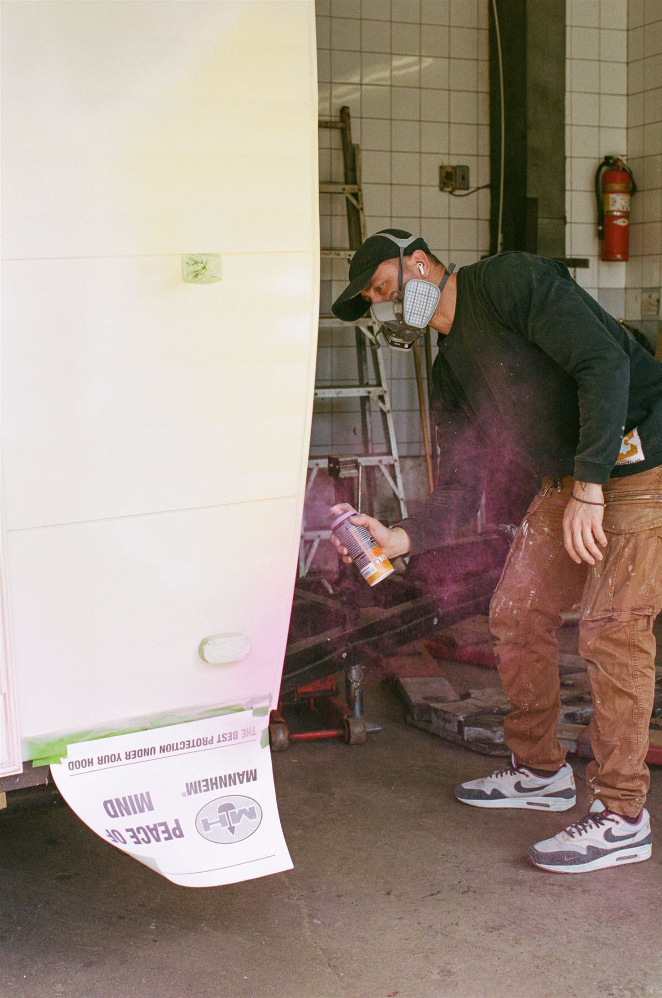 Person using a spray can in a workshop setting with a poster on the wall.