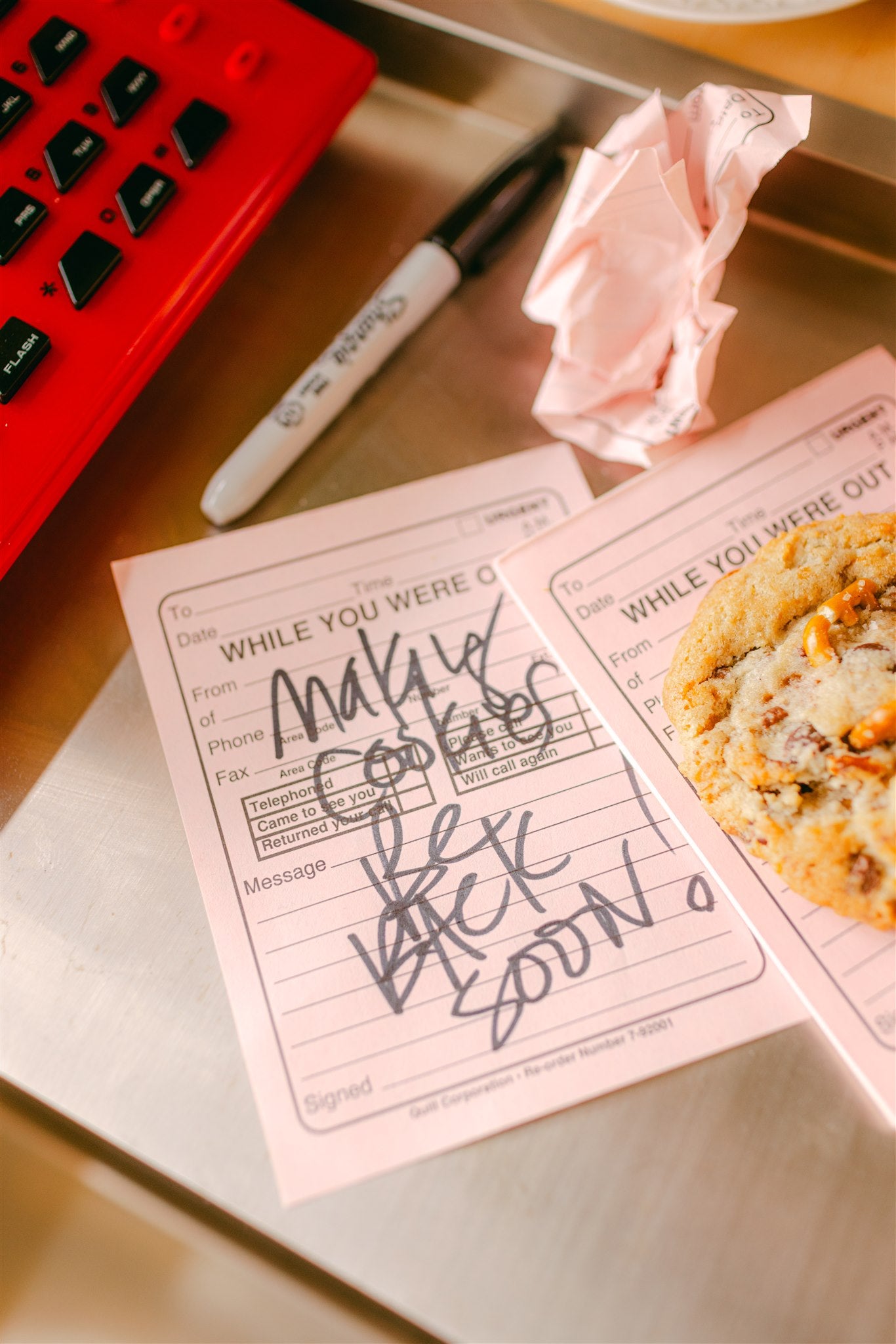 Notebook with a cookie and a crumpled pink note on a desk
