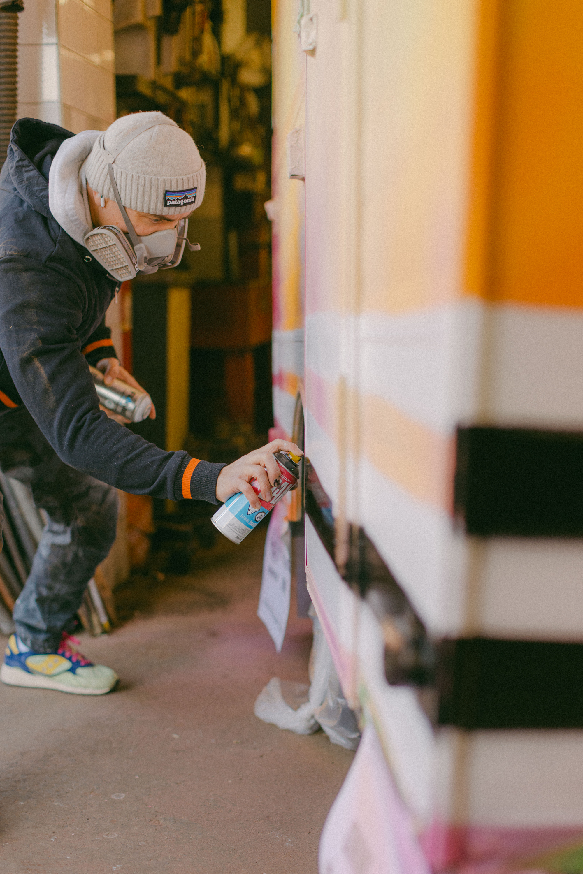 Person spray painting a colorful striped wall.