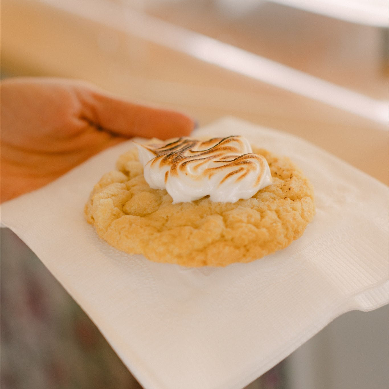 Cookie with toasted marshmallow on a piece of paper, held by a hand.