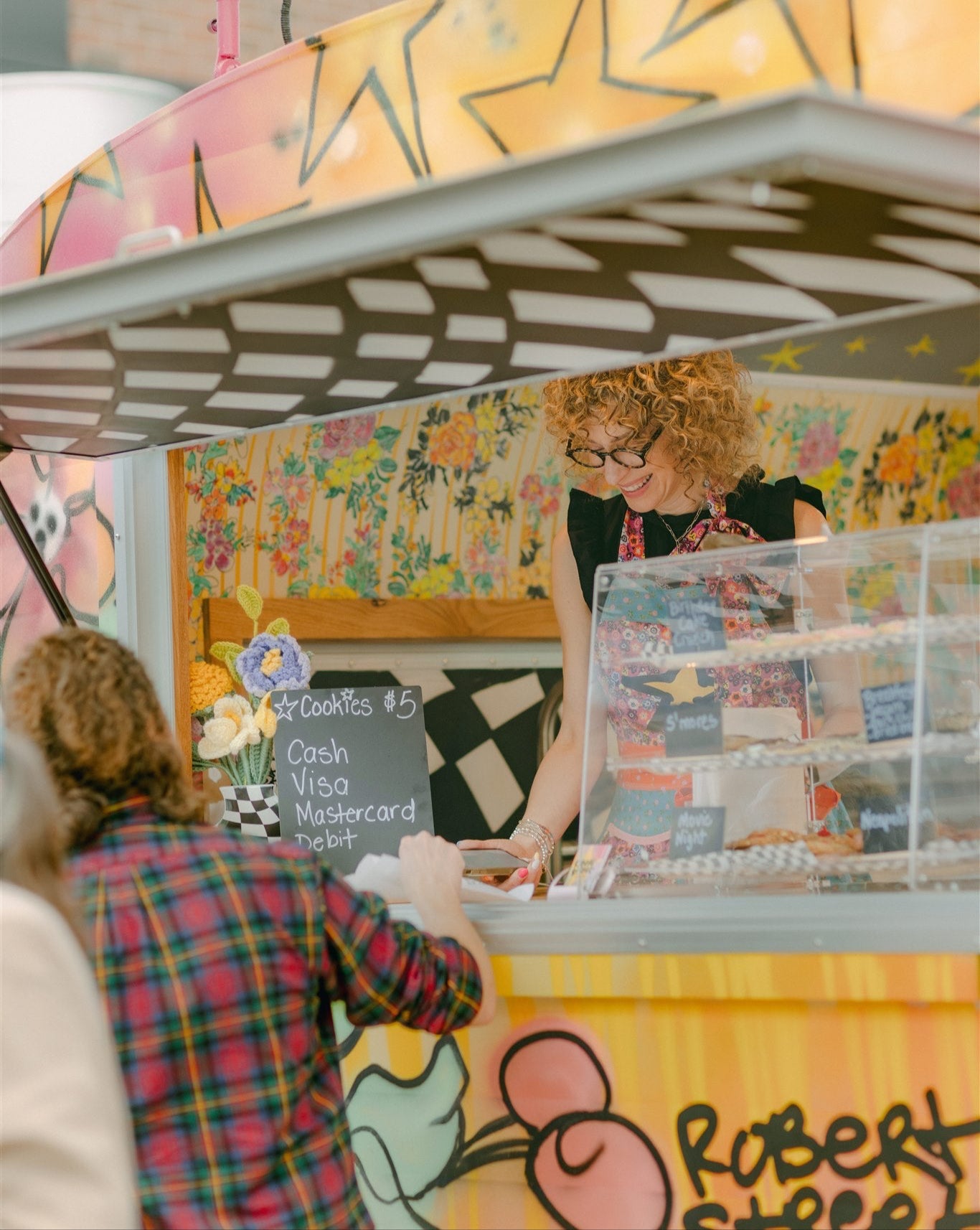 Person ordering at a colorful food stand with a customer.